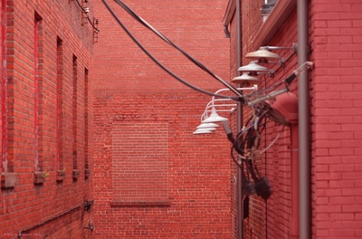 A bright red photo of a brick alleyway with lights ensconced on one wall and bricked up windows on the other walls.